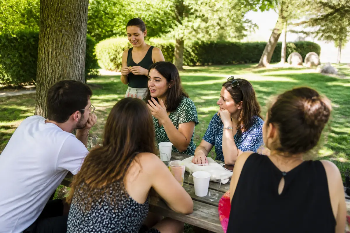 Groupe discutant autour d'une table de pique-nique sous les arbres, un sourire de leur part